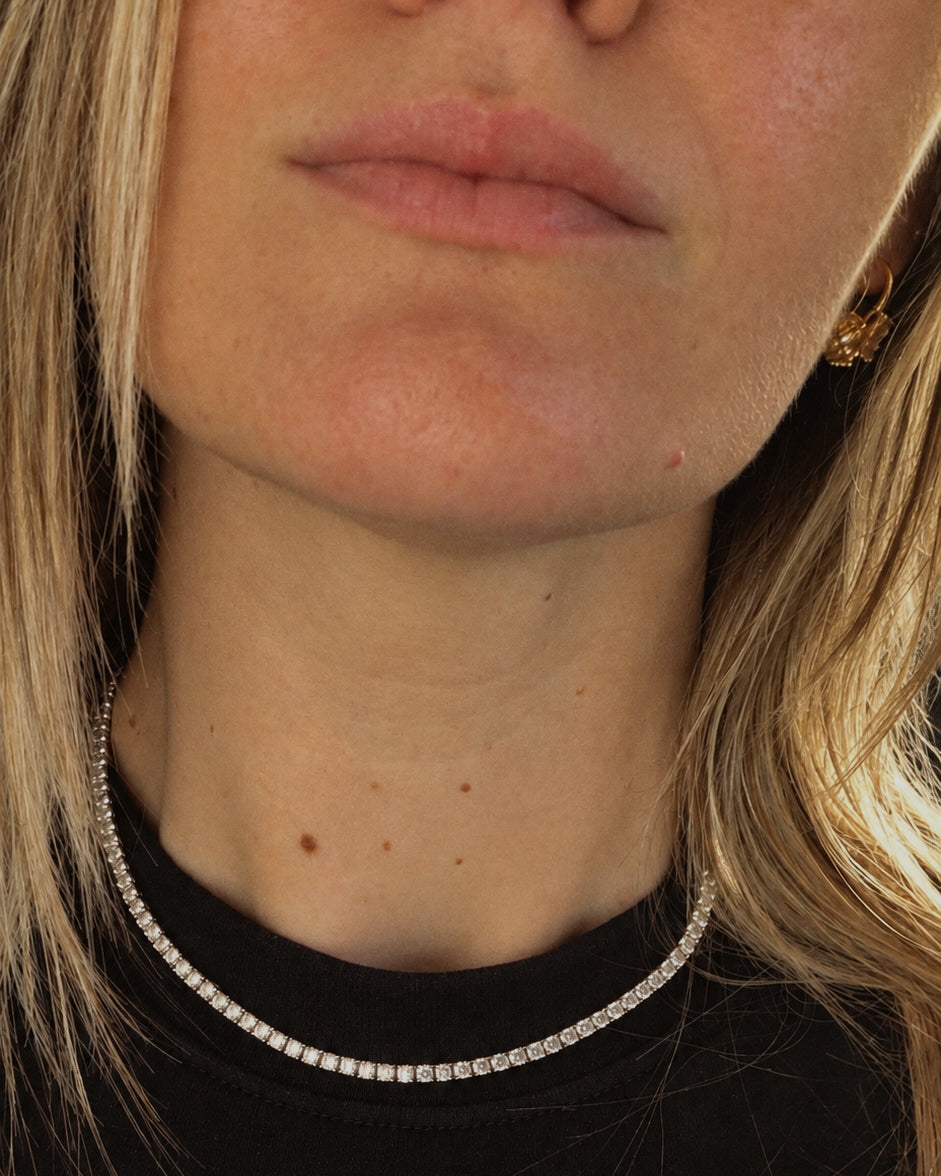 Close-up of a silver tennis necklace worn with a black top.