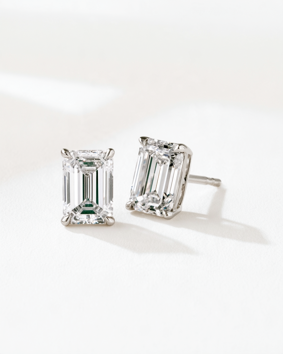 A pair of emerald-cut diamond stud earrings in a silver-toned setting, displayed on a clean white surface with soft shadows.