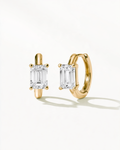 A pair of gold huggie hoop earrings with rectangular emerald-cut clear gemstones, displayed on a clean white background with soft shadows.