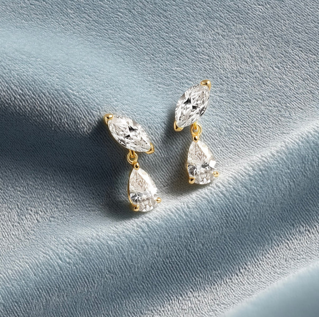 Pair of Lenny marquise and pear drop earrings on a blue-grey surface.