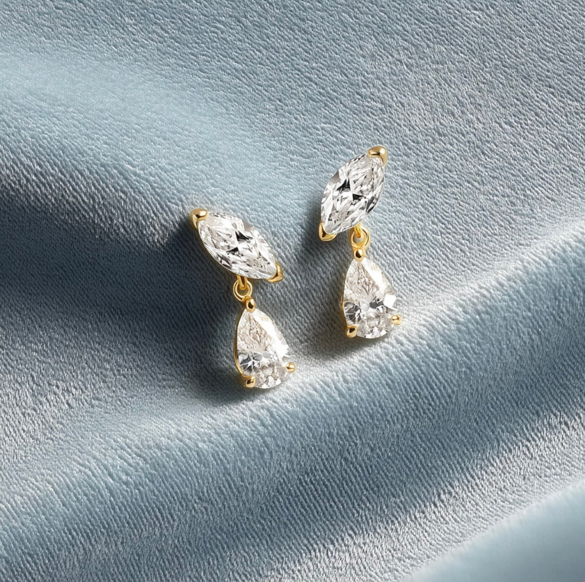 Pair of Lenny marquise and pear drop earrings on a blue-grey surface.