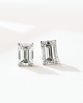A pair of emerald-cut diamond stud earrings in silver-toned settings, displayed on a clean white surface with soft shadows.