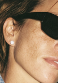 Round moissanite stud earring worn on the ear with black sunglasses.