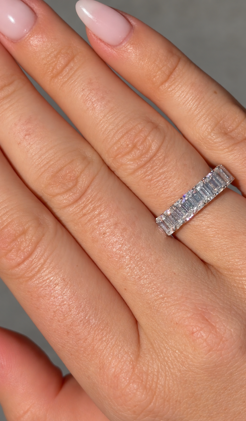 Emerald Half Eternity Band worn on a hand, showing the emerald-cut moissanite stones and rhodium plated sterling silver setting.